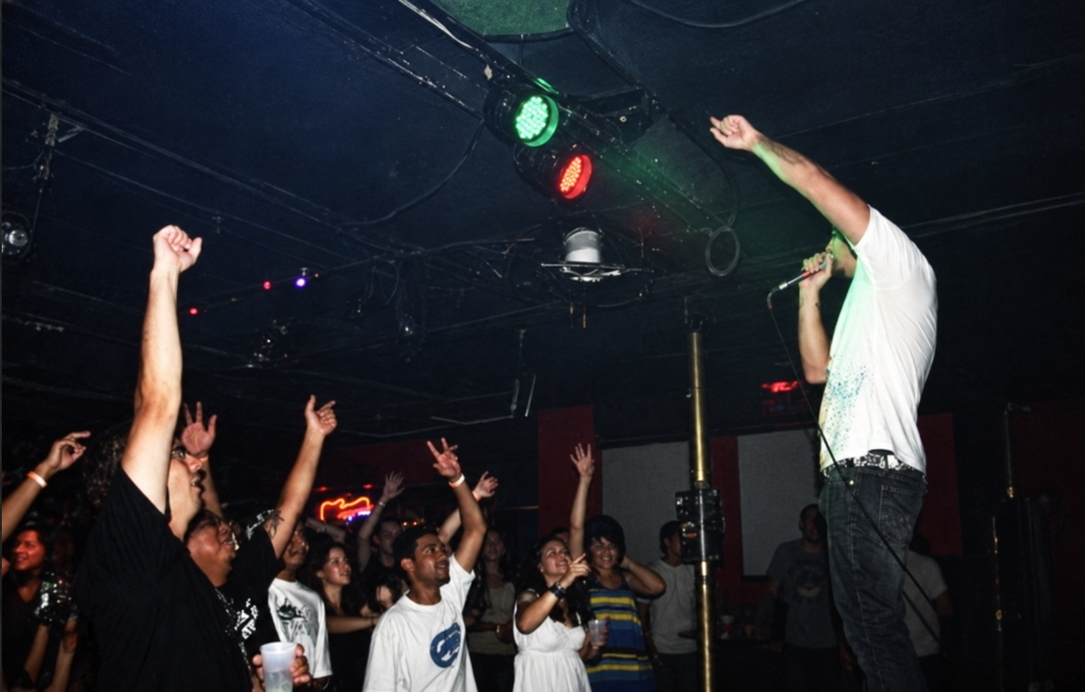 Bear the Astronot performing to a crowd with his arm raised beneath colored stage lights